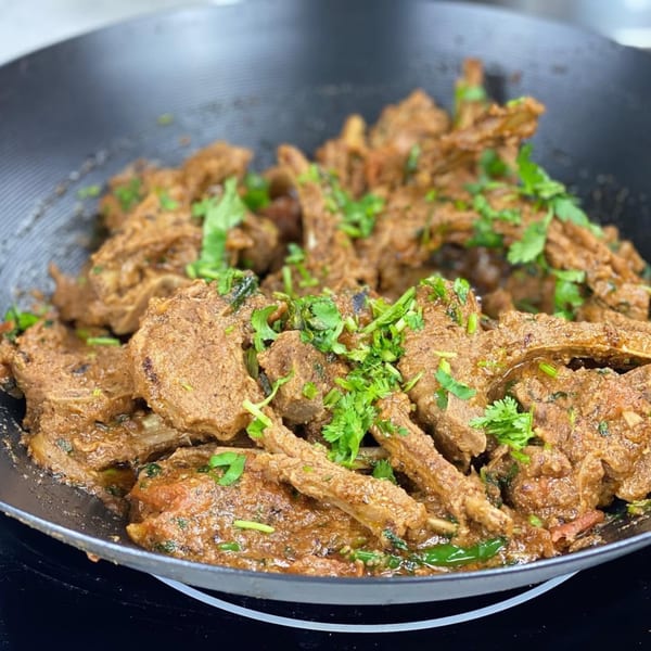 Indian lamb chops in a rich brown sauce, garnished with fresh green cilantro in a black pan.