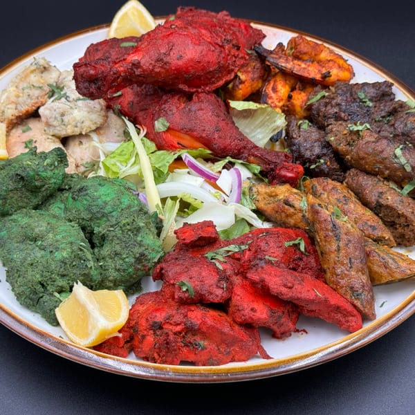 A large platter of various Indian grilled meats, including red tandoori chicken, green chicken, and kebabs.
