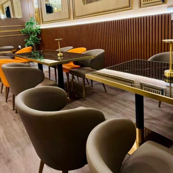 Modern dining area with dark tables, gold accents, and a mix of orange and gray chairs.