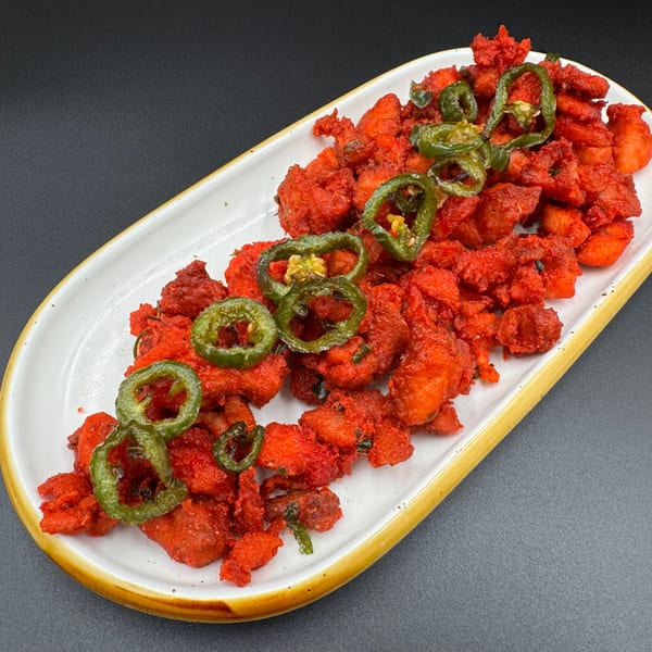 Khan's Kitchen's bright red Indian chicken 65, garnished with green chili slices on a white platter.