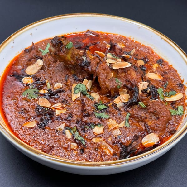 Khan's Kitchen Indian chicken curry, garnished with sliced almonds and fresh cilantro, in a white bowl.