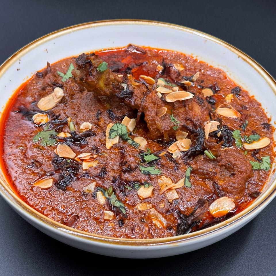 Khan's Kitchen Indian chicken curry, garnished with sliced almonds and fresh cilantro, in a white bowl.