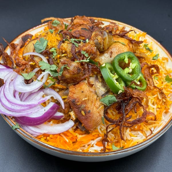 Khan's Kitchen chicken biryani with rice, fried onions, sliced red onions, and green chilies.
