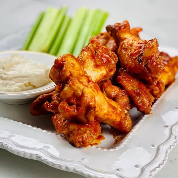 Spicy chicken wings with a side of creamy dip and celery sticks on a white plate.