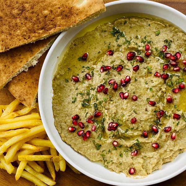 A bowl of Indian baba ghanoush with pomegranate seeds, parsley, naan bread, and fries.