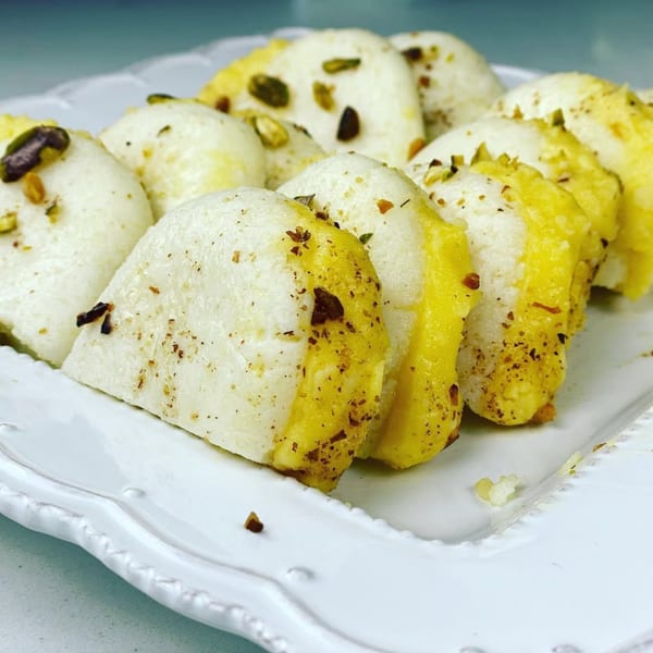 A white plate holds several pieces of Indian dessert, some topped with pistachios and spices.