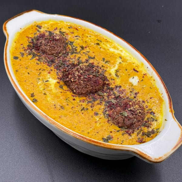 Khan's Kitchen Indian dish with three brown meatballs in a rich orange sauce, garnished with herbs.
