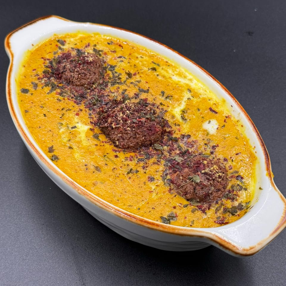 Khan's Kitchen Indian dish with three brown meatballs in a rich orange sauce, garnished with herbs.