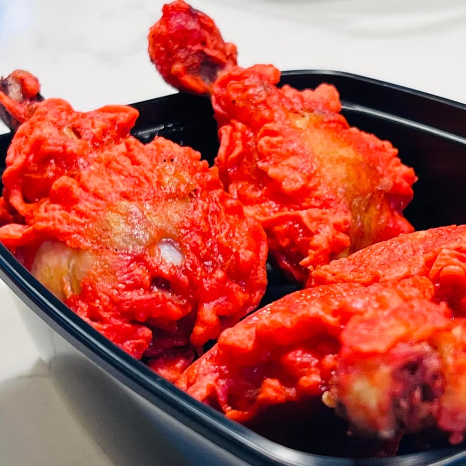 Bright red Indian chicken lollipops, coated in sauce, served in a black container.