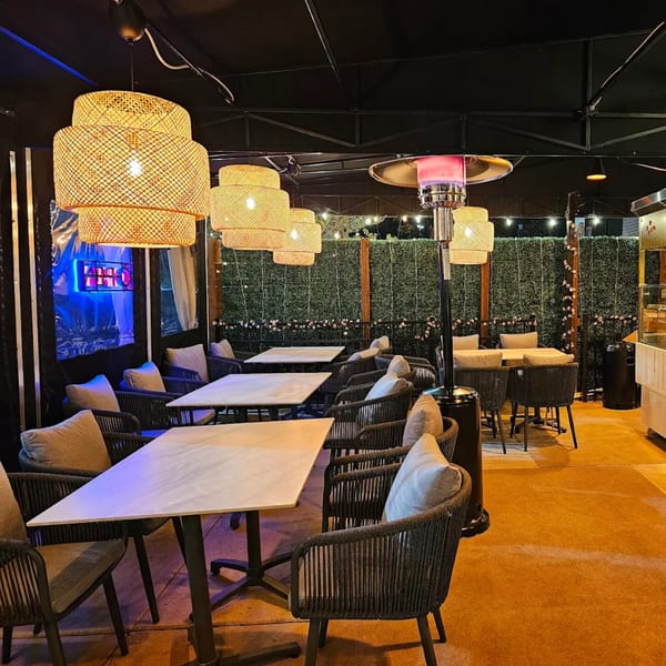 Outdoor dining area at Khan's Kitchen with rattan lamps, patio heaters, and green wall decor.