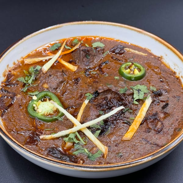 Khan's Kitchen's Indian curry, garnished with green chilies, ginger strips, and fresh cilantro.